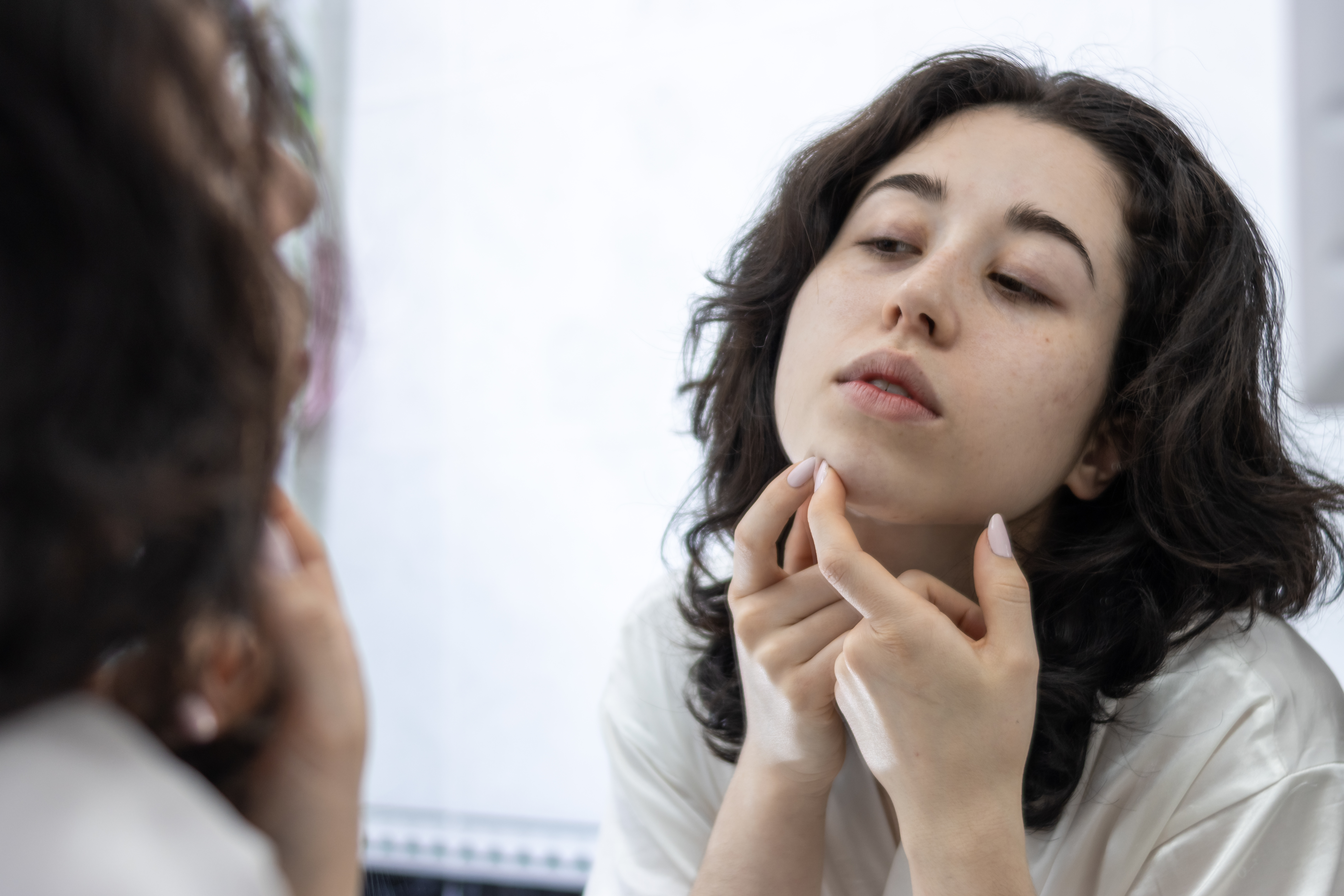 unhappy-latin-lady-white-bathrobe-front-mirror-bathroom-remove-blackheads-from-her-face.jpg